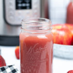 Front view of a mason jar with strawberry applesauce with an instant pot in the background.
