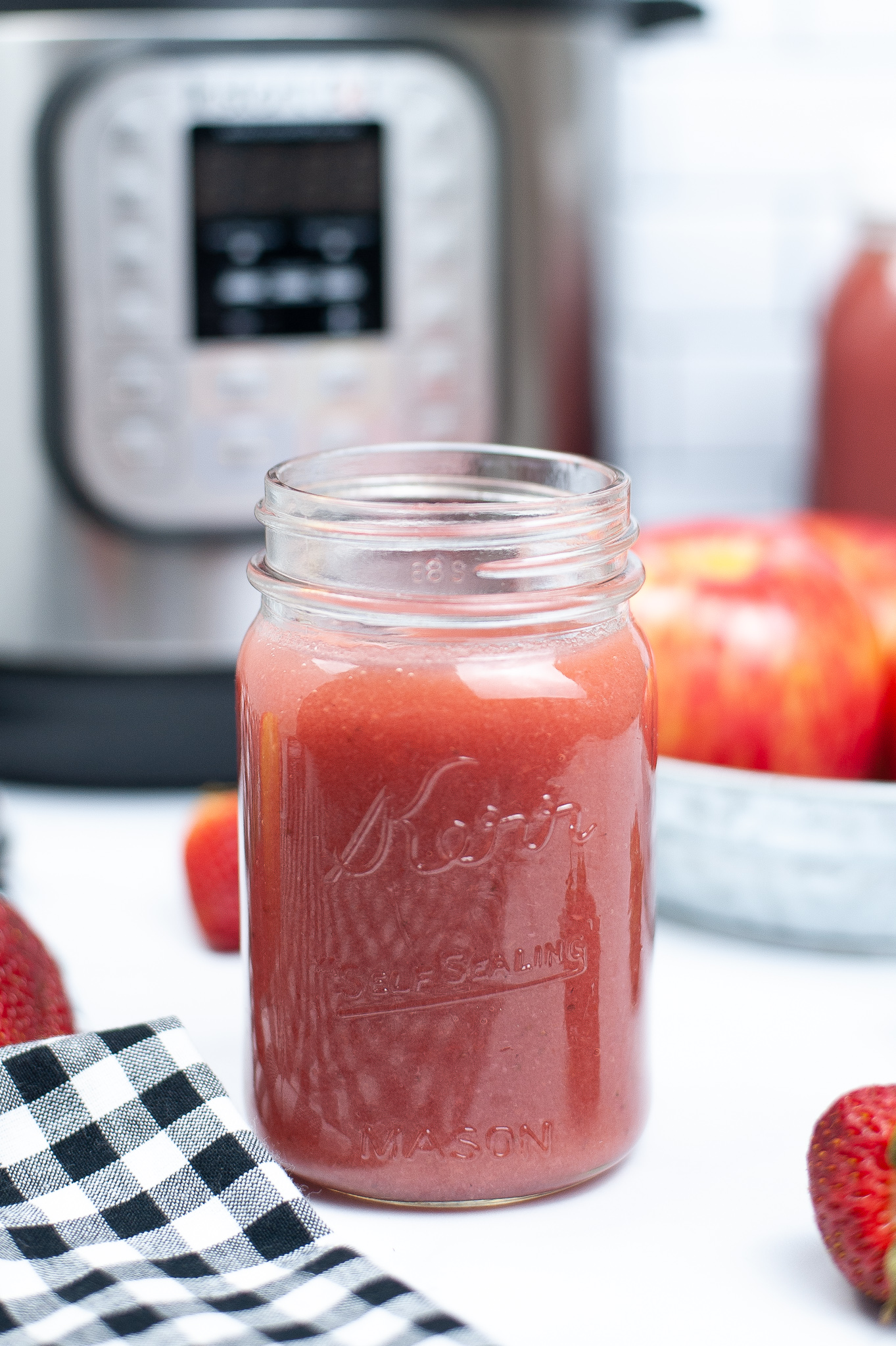 Front view of a mason jar with strawberry applesauce with an instant pot in the background.