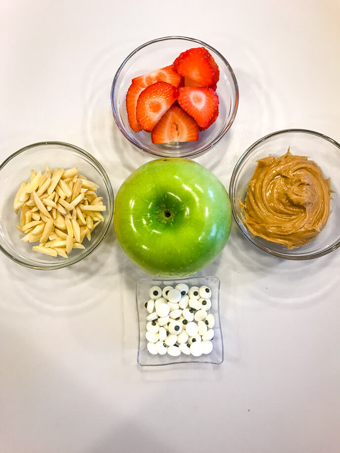 Clear bowls of apple, eye, strawberries and peanut butter.
