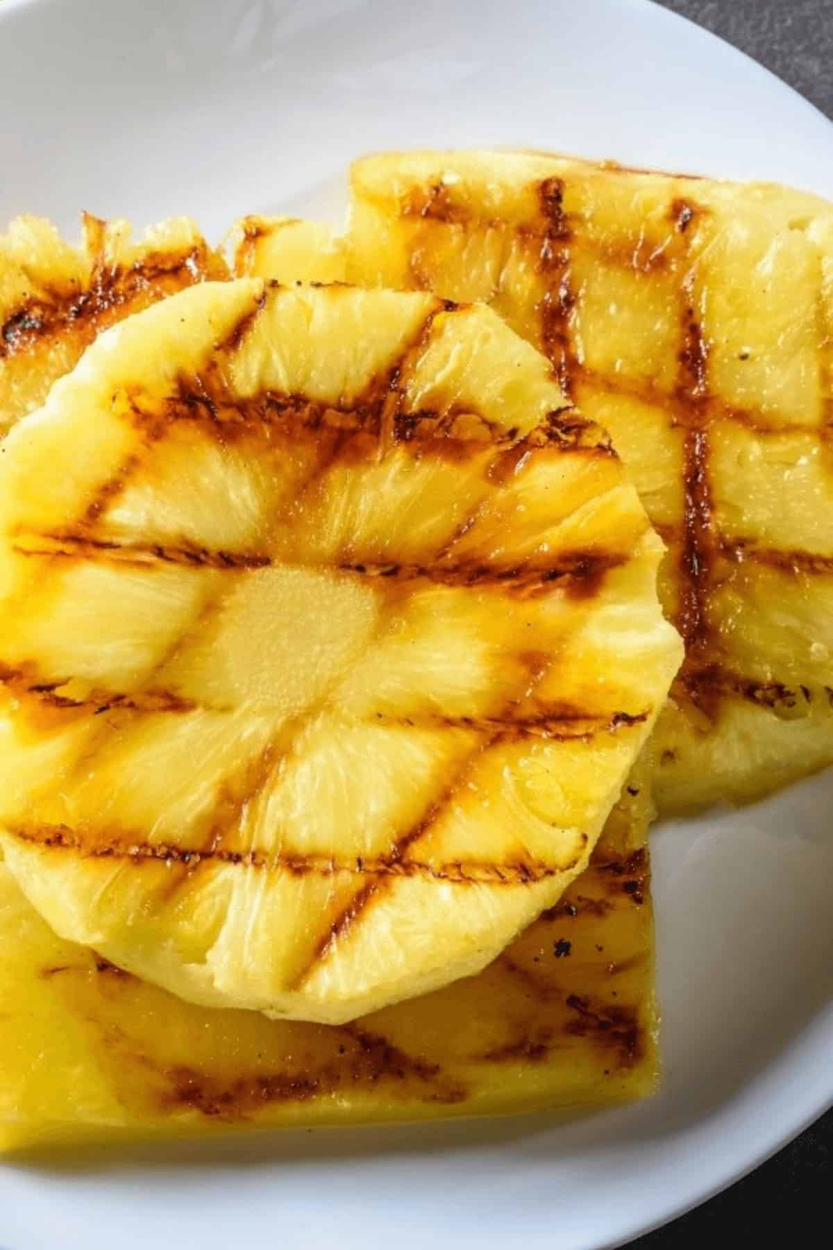 Two grilled pineapple slices with perfect char marks rest invitingly on a white plate.