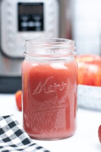 A jar of delicious instant pot strawberry applesauce with an instant pot in the back.
