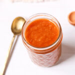 A jar of peach bbq sauce with a spoon.