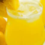 A glass of pineapple lemonade with a wedge of pineapple on it.