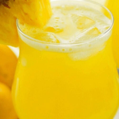 A glass of pineapple lemonade with a wedge of pineapple on it.