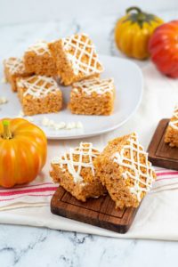 Pumpkin Rice Krispie Treats on a wooden dish, and on a round plate and with a pumpkin.