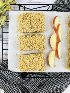 Three Apple Crisp Bars on a white plate with sliced apples.