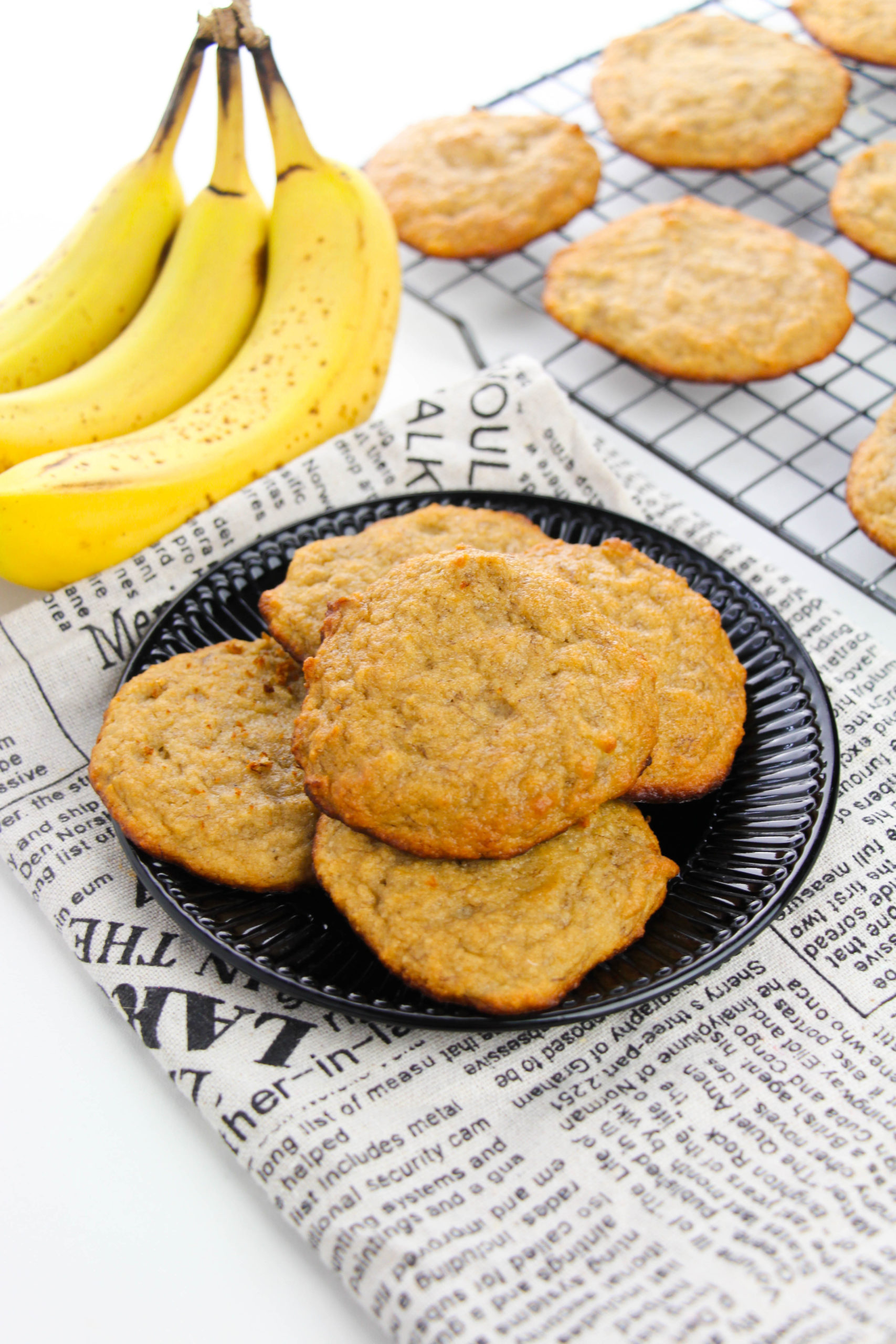A stack of five banana bread cookies on a plate wih a bunch of bananas on the side.