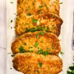 Square white plate with breaded baked pork chops sprinkled with herbs.