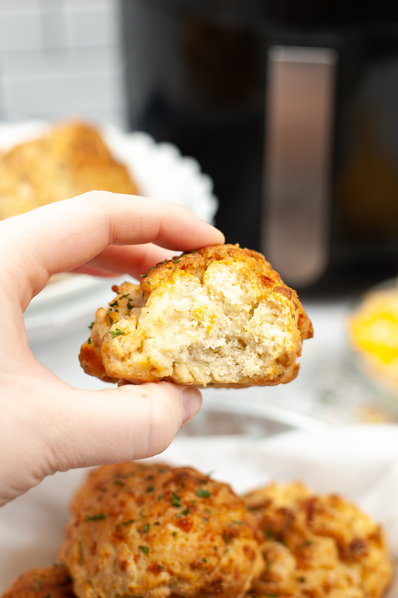 Hand holding a Air Fryer Cheddar Bay Biscuits with a plate underneath.