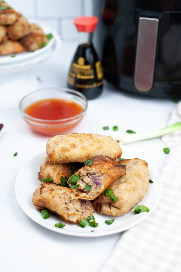 Air Fryer Chicken Egg Rolls on a rounds white plate with a side of dipping sauce.