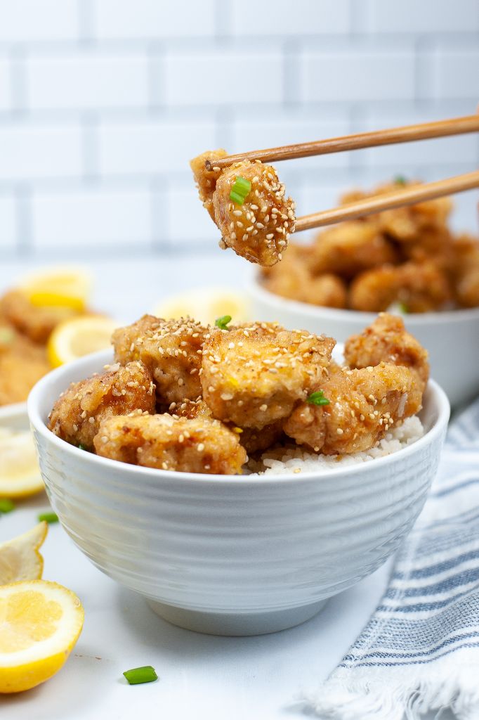 Side view of a bowl of lemon chicken. With a piece on chop sticks.