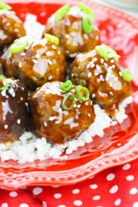 Honey Garlic Meatballs over rice on a red scalloped plate with a red and white dot tablecloth.