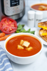 White crock of Instant Pot tomato soup with croutons on top.