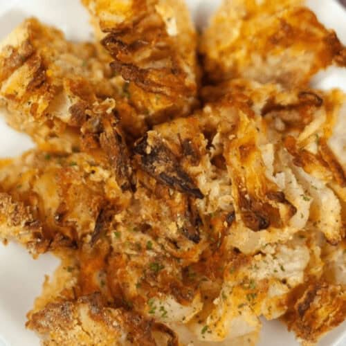 A plate of crispy, golden brown air fryer blooming onions, lightly seasoned and artfully piled on a white dish.