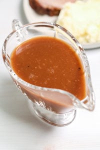 Beef Brown Gravy in a gravy boat with dinner plate in background.