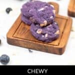 Delight in blueberry white chocolate cookies, brimming with juicy blueberries and creamy white chocolate chips, elegantly arranged on a wooden tray and accompanied by scattered berries.
