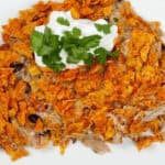 A plate of the dish is topped with crushed orange chips, a dollop of sour cream, and cilantro.