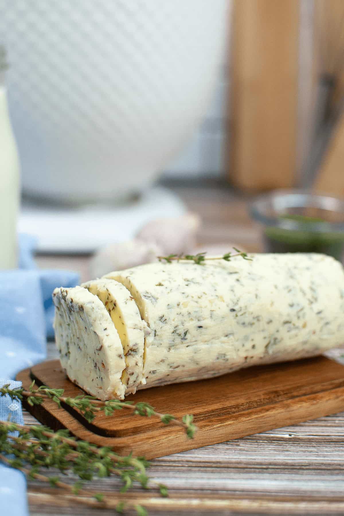 A roll of garlic herb butter rests on a wooden board, with a slice cut from one end and garnished with fresh herbs.