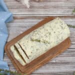 A block of garlic herb butter rests on a wooden board, surrounded by fresh thyme sprigs and garlic bulbs, against a rustic wooden background.