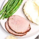A plate with two slices of meat roast, mashed potatoes, and cooked green beans.