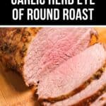 Sliced beef eye of round roast with garlic and herbs rests on a wooden cutting board, revealing a tender, pink interior and perfectly seasoned crust.