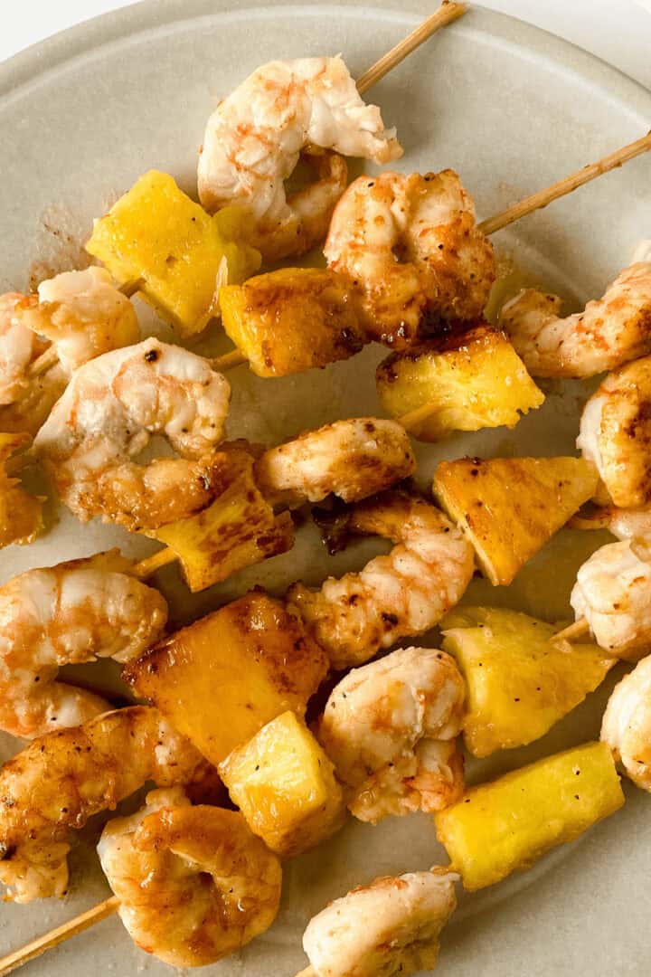 Hawaiian Garlic Shrimp Skewers and pineapple served on a light-colored plate.