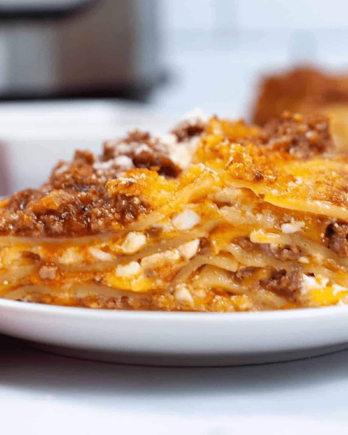 A plate of instant pot lasagna on a table next to an Instant Pot, ready to be served.