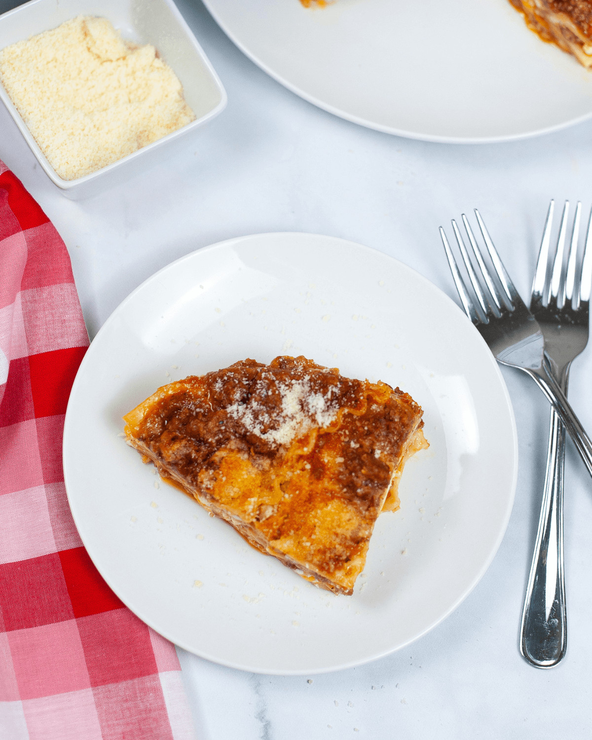 A slice of lasagna on a plate next to a fork, tempting and delicious.
