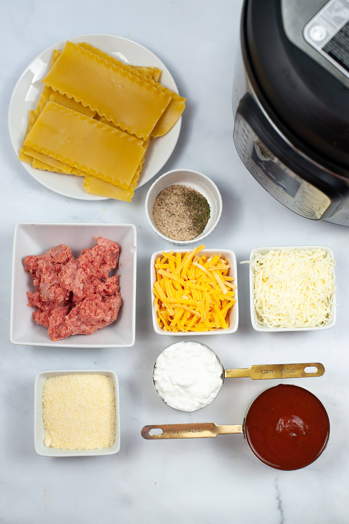 Ingredients for the meal are displayed on a white table. Ground beef, cheese, noodles and sauce.