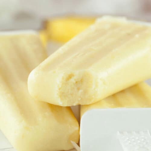 A close-up image of homemade creamy pineapple popsicles on a white surface with bright lighting.