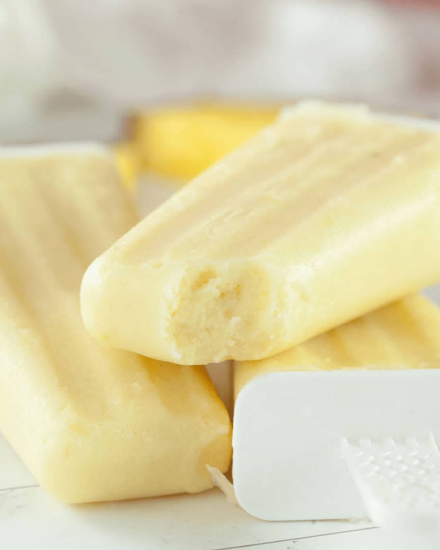 A close-up image of homemade creamy pineapple popsicles on a white surface with bright lighting.