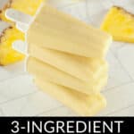 Stack of homemade pineapple popsicles with fresh pineapple slices in the background, on a marble surface. Text above reads "3-ingredient pineapple popsicles.