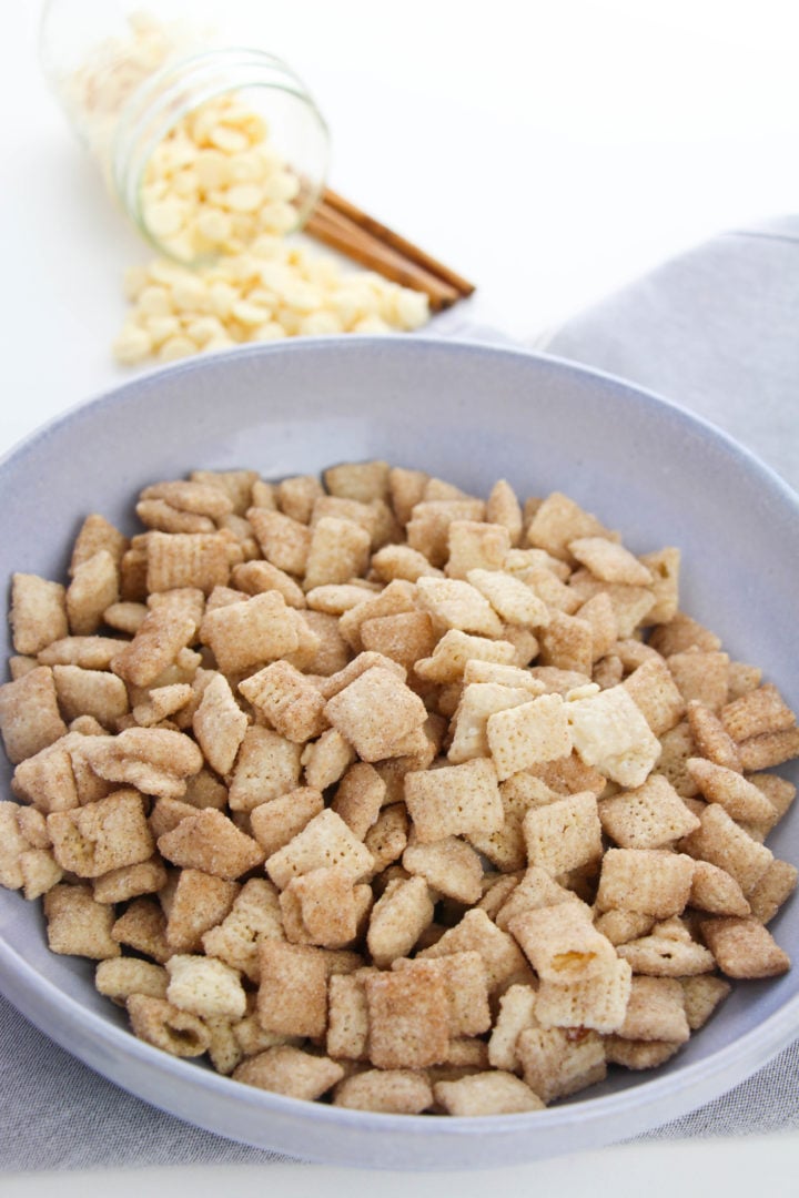 Blue bowl of churro muddy buddies with a cinnamon stick on the side.