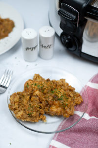 Crock Pot Chicken Stuffing Casserole on a clear plate with salt and pepper and crock pot in the background.