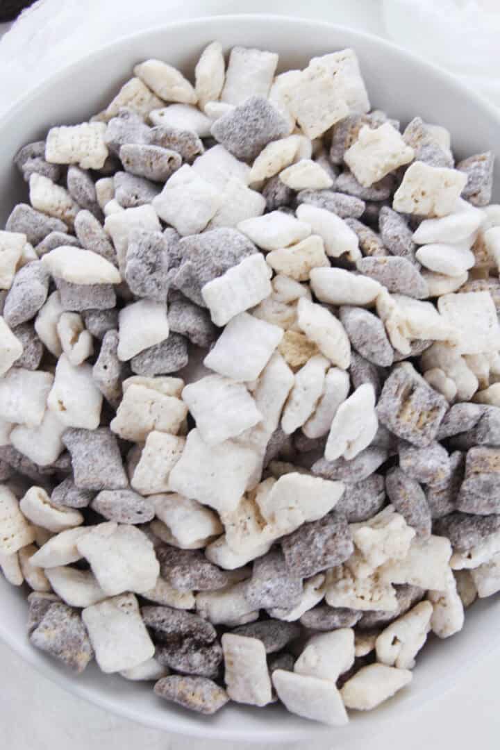 A bowl filled with Cookies and Cream Chex Mix showcases cereal squares in shades of white, gray, and light brown.