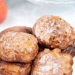 A plate of delicious homemade apple fritters, perfectly glazed, stacked on a pristine white surface.
