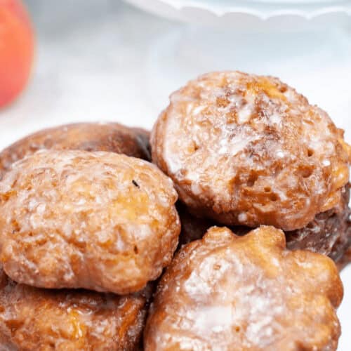 A plate of delicious homemade apple fritters, perfectly glazed, stacked on a pristine white surface.