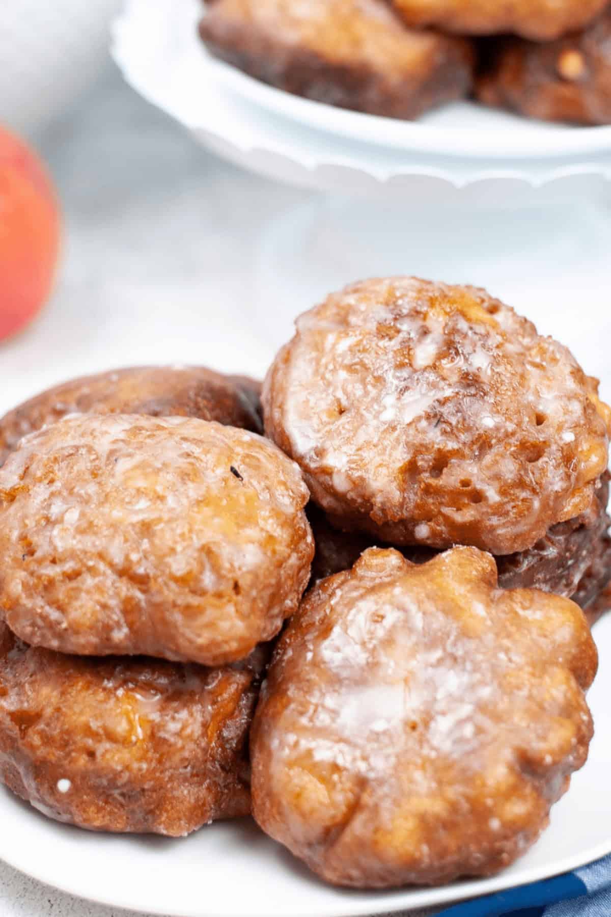 A plate of delicious homemade apple fritters, perfectly glazed, stacked on a pristine white surface.