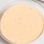 A glass bowl containing creamy, light orange dipping sauce with specks, reminiscent of an In n Out sauce recipe, placed on a white surface.