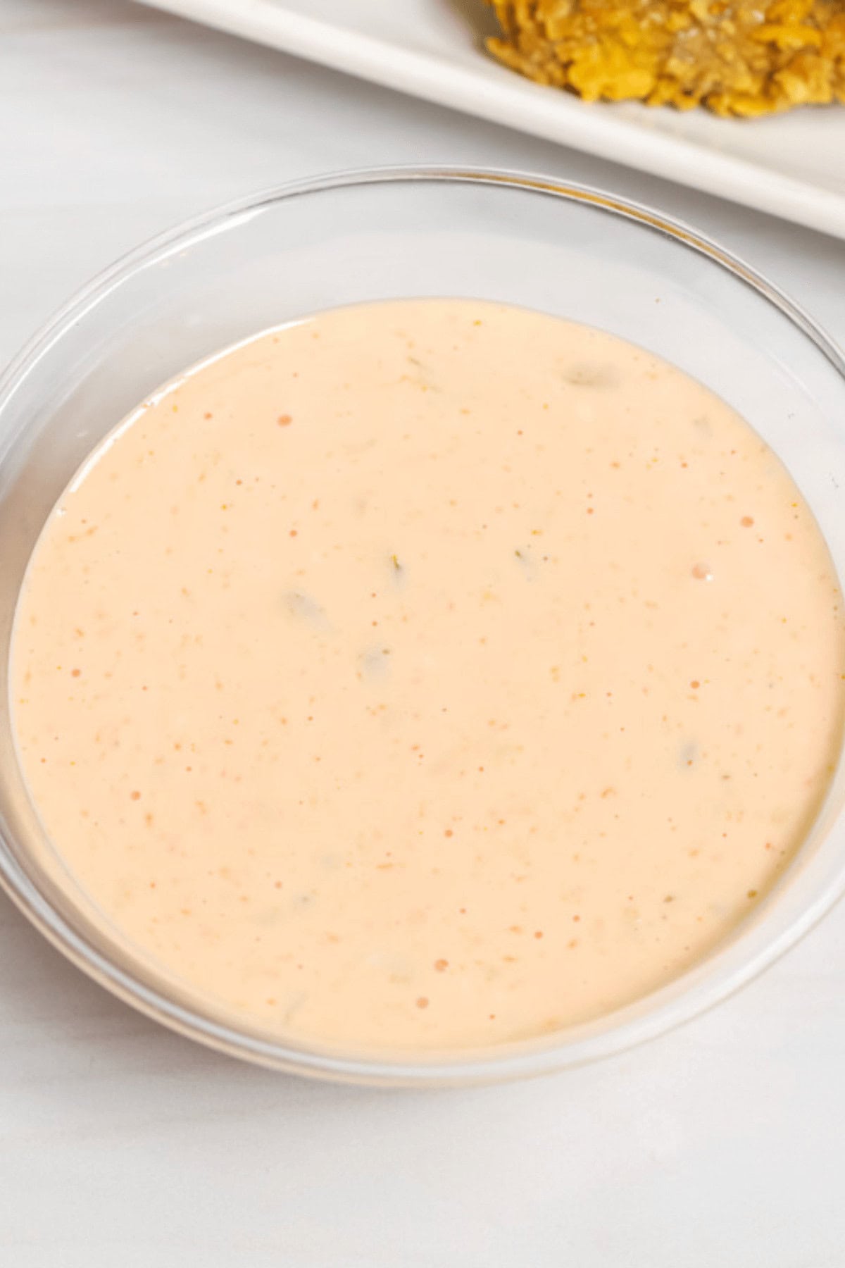 A glass bowl containing creamy, light orange dipping sauce with specks, reminiscent of an In n Out sauce recipe, placed on a white surface.