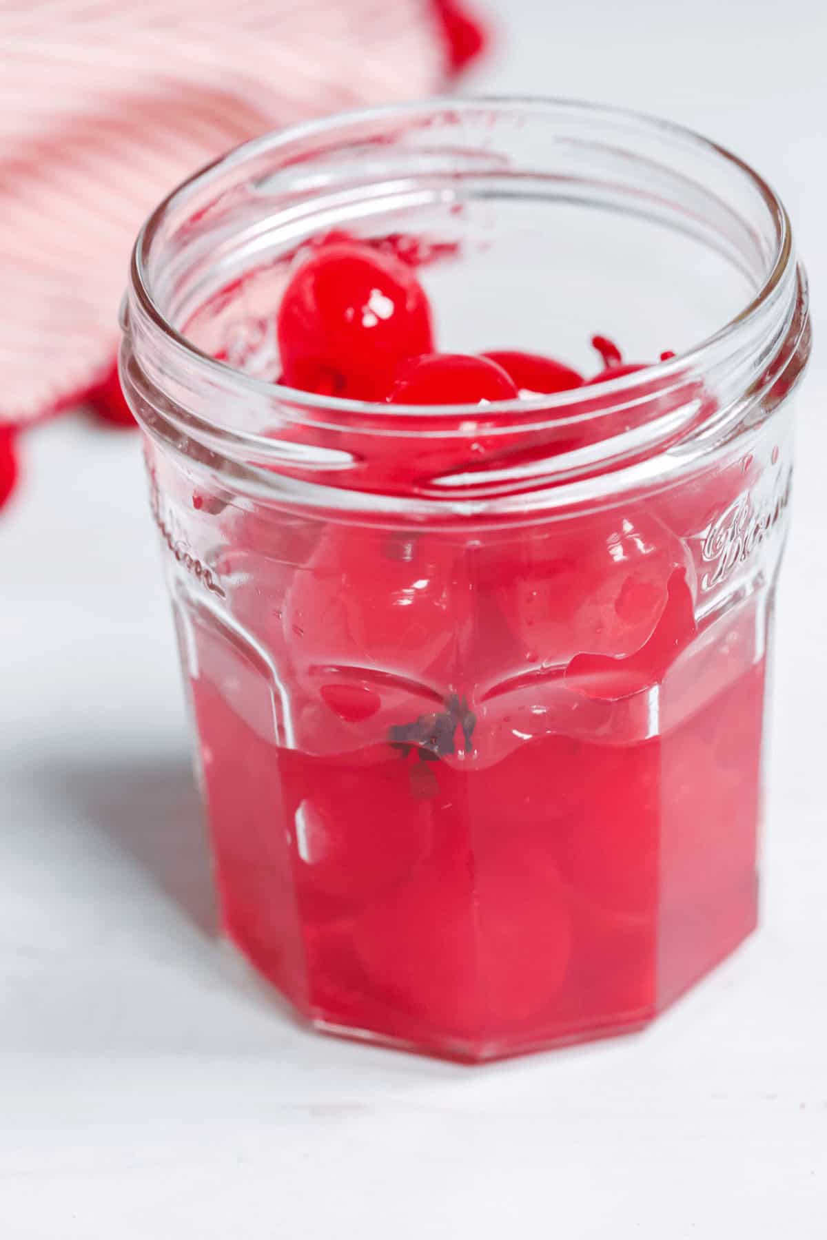 A glass jar brimming with bright red fruit infused in syrup.