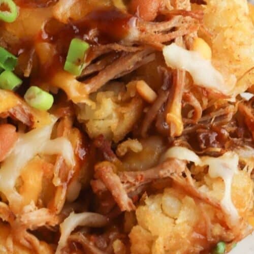 Close-up of a plate with shredded meat, melted cheese, tater tots, barbecue sauce, and chopped green onions—perfect for trying out a new totchos recipe.