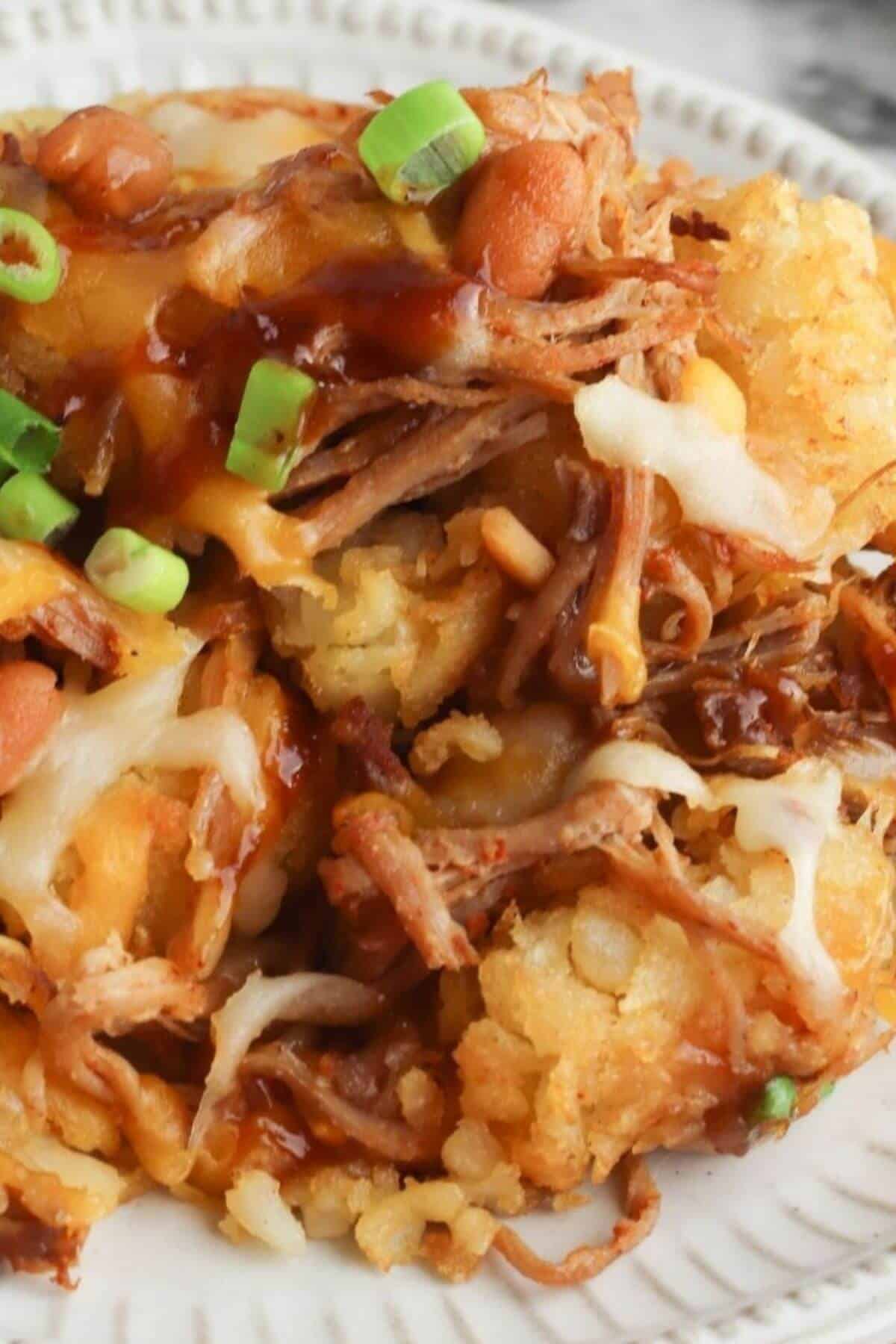 Close-up of a plate with shredded meat, melted cheese, tater tots, barbecue sauce, and chopped green onions—perfect for trying out a new totchos recipe.