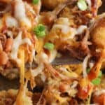Close-up of the recipe featuring tater tots topped with shredded meat, melted cheese, barbecue sauce, beans, and chopped green onions.