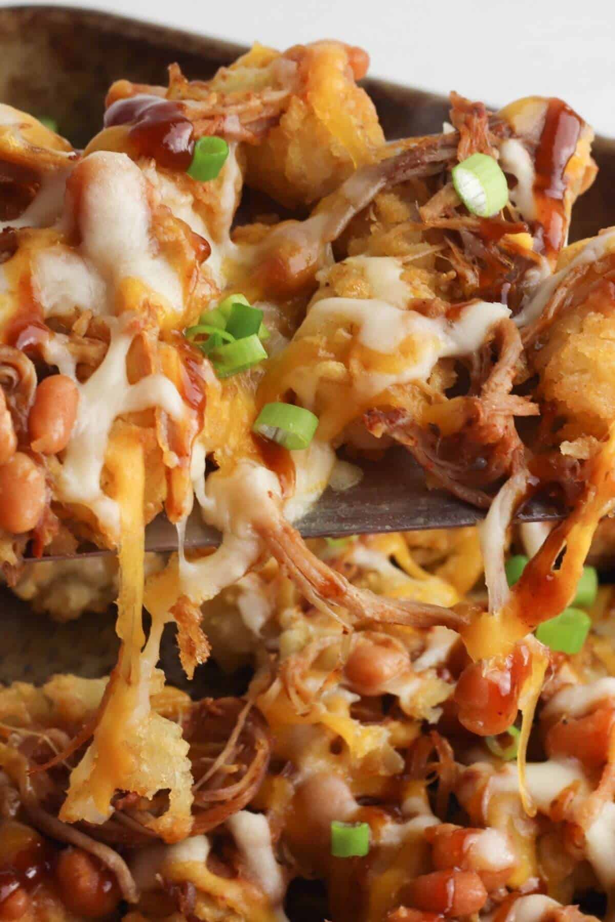 Close-up of the recipe featuring tater tots topped with shredded meat, melted cheese, barbecue sauce, beans, and chopped green onions.
