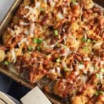 A baking pan filled with with shredded meat, beans, melted cheese, barbecue sauce, and green onion.