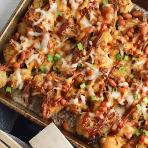 A baking pan filled with with shredded meat, beans, melted cheese, barbecue sauce, and green onion.