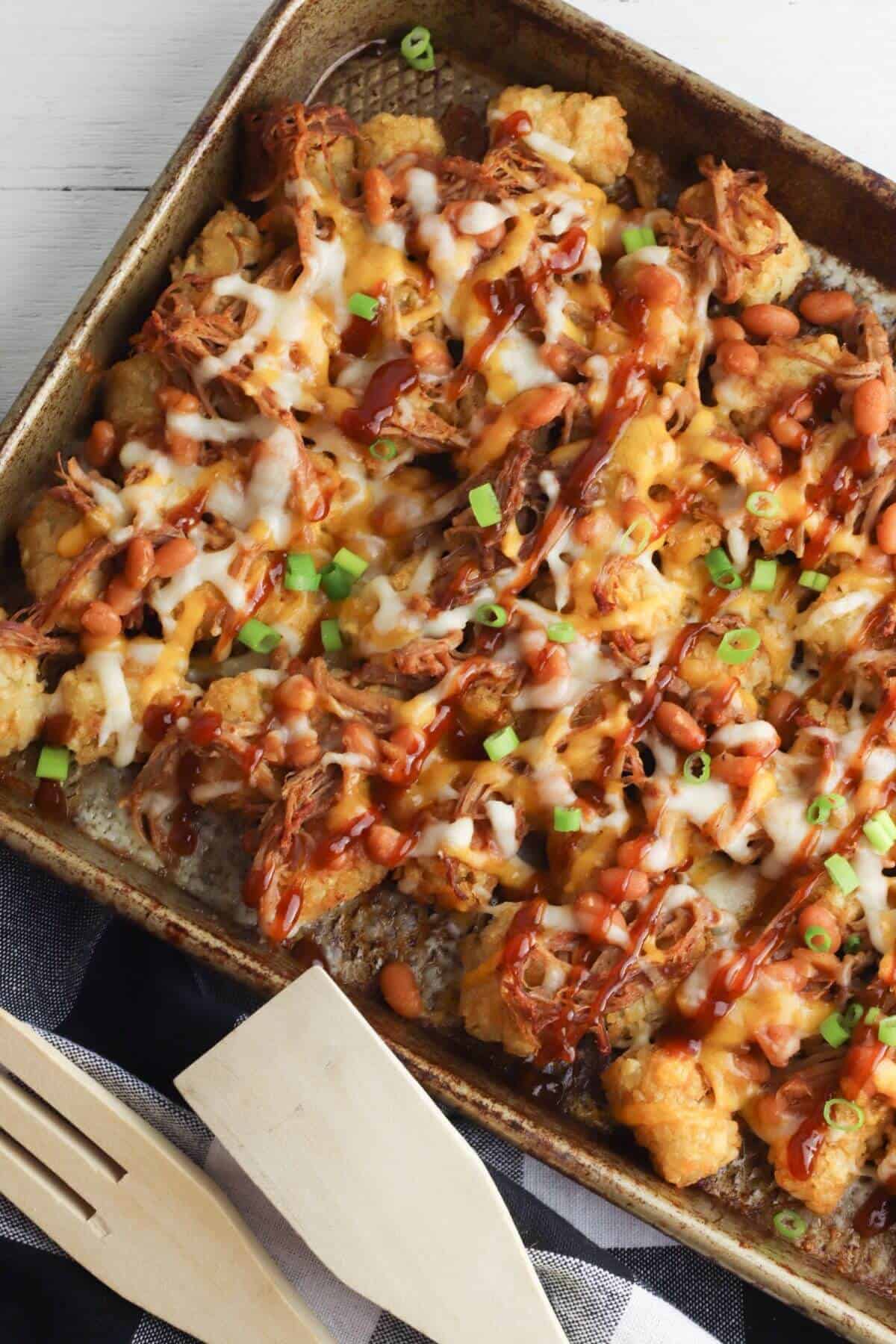 A baking pan filled with with shredded meat, beans, melted cheese, barbecue sauce, and green onion.