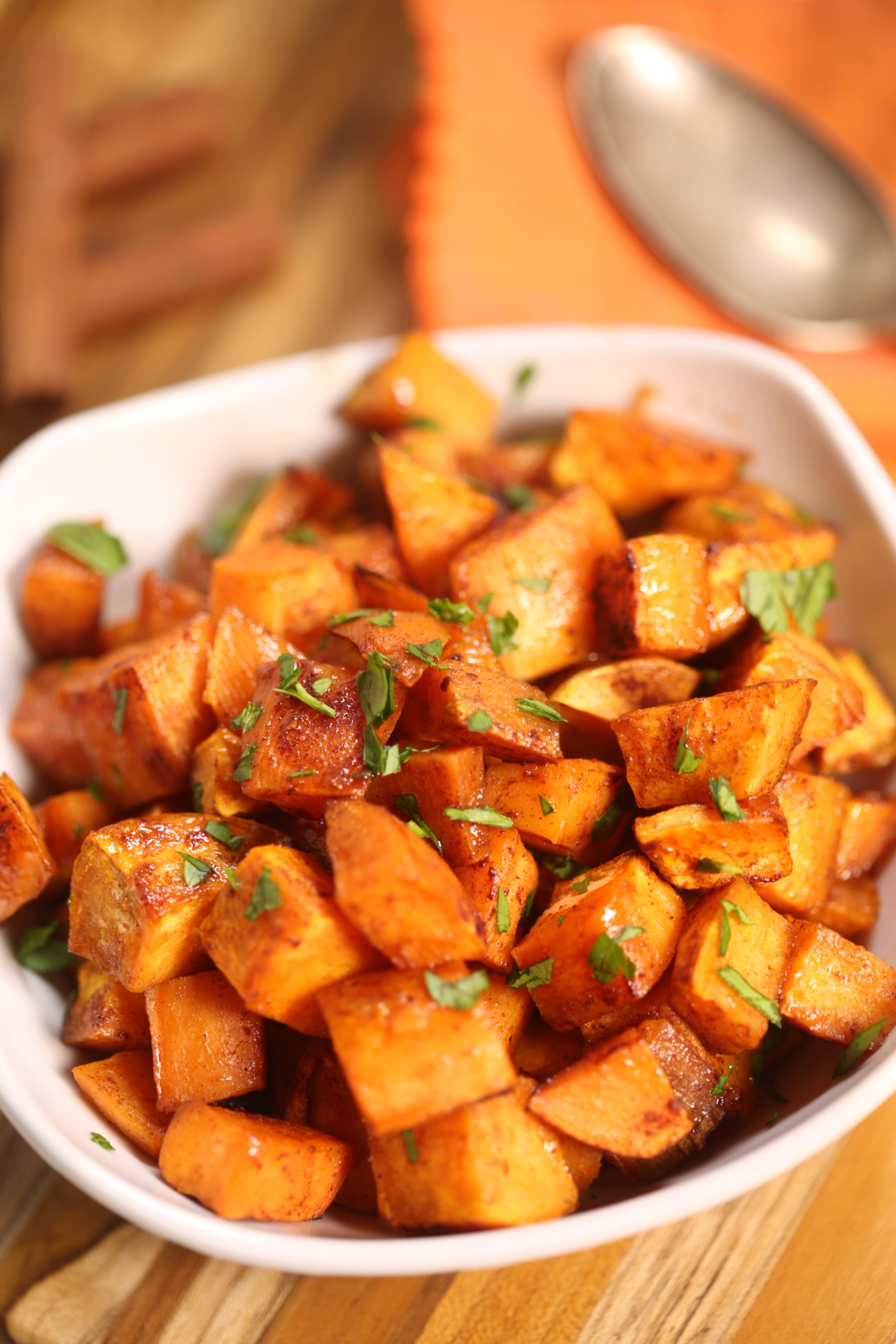 Crispy roasted sweet potatoes in a white bowl with herbs on top and a spoon in the background.