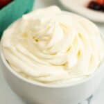 A white bowl sits on a table near a basket of berries.
